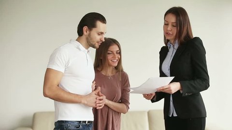 Young attractive happy smiling casual couple meeting consultant in office or at home. Cheerful husband and wife discussing contract and shaking hands with female contractor after reaching an agreement