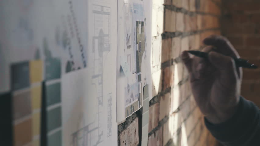 Stylish and modern cabinet in the loft style: A brick wall with notes and blueprints. Drawings and diagram of future buildings on the wall, there is blueprints and model house on the wall