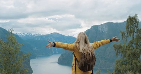 Woman with arms raised on top of mountain looking at view of fjords lifting arm up celebrating scenic landscape from high up enjoying Norway vacation travel adventure nature background view