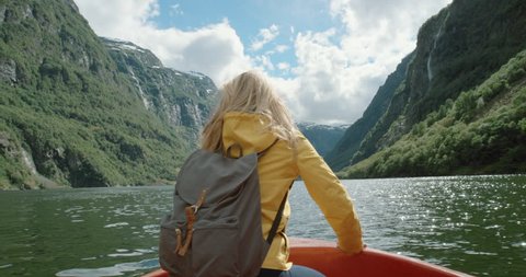 Woman lifting arms up sitting in boat on Fjord Norway hair blowing in wind celebrating scenic landscape nature background view enjoying vacation travel adventure