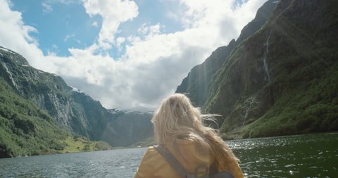 Woman sitting in boat on Fjord Norway hair blowing in wind traveling towards scenic landscape nature background view enjoying vacation travel adventure