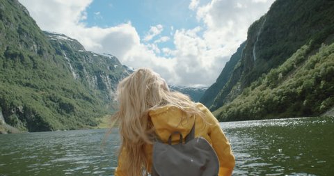 Woman sitting in boat on Fjord Norway hair blowing in wind traveling towards scenic landscape nature background view enjoying vacation travel adventure