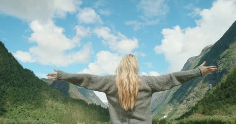 Woman with arms raised on top of mountain looking at view lifting arm up celebrating scenic landscape enjoying vacation travel adventure nature Norway