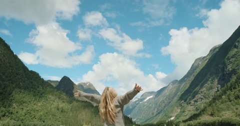 Woman with arms raised on top of mountain looking at view lifting arm up celebrating scenic landscape enjoying vacation travel adventure nature Norway