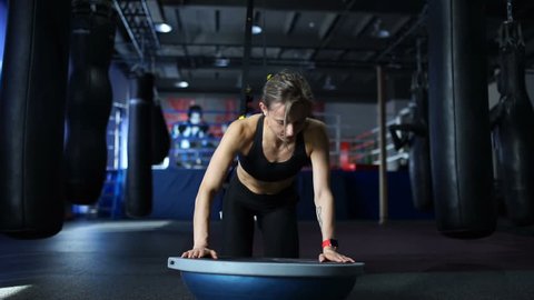  Fit woman in black sportswear doing push UPS on the Bosu and the TRX in gym