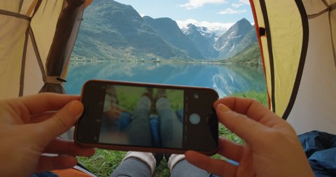 Camping woman lying in tent taking photo of feet with smart phone Close up of Girl wearing hiking boots relaxing on vacation POV Norway