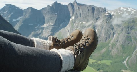 Close up hiking boots of Independent Woman traveller on top of mountain looking at view Hiker girl dangling feet over edge of cliff enjoying vacation travel adventure nature Romsdal Valley Norway