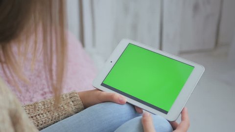 Woman using horizontal tablet computer with green screen. Close up shot of woman's hands with pad. 