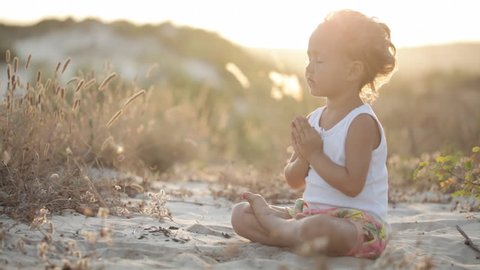 Little cute girl meditates on the sand dunes at sunset with beautiful natural light.