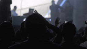 Silhouette of people holding their hands up at a concert. Blured musicians