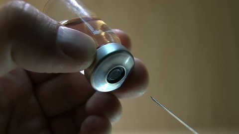 Doctor With Syringe Needle Pierces The Rubber Stopper Of The Glass With Medication Vial On A Light Background
