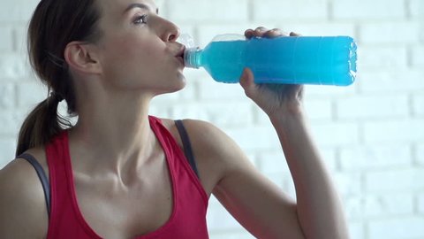 Young woman drinking isotonic drink after workout at home

