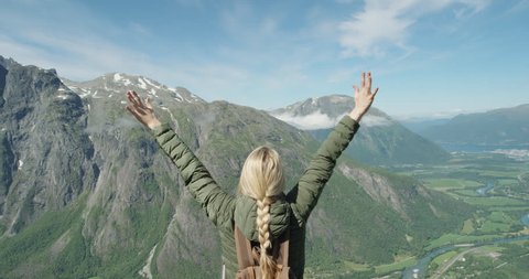 Independent Woman traveller with arms raised on top of mountain looking at view Hiker girl lifting arm up celebrating scenic landscape enjoying vacation travel adventure nature Romsdal Valley Norway
