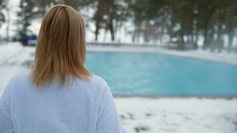 Young blonde woman goes to outdoor swimming pool and undressing at winter day