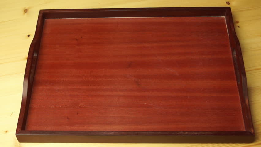 A large number of small dried fish falls on the wooden tray.