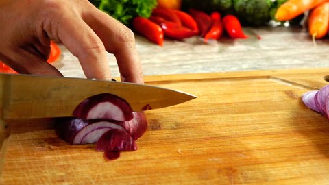 Closeup of chef hands slicing red onion on wooden board in slow motion