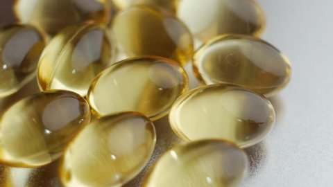 Omega 3 gold fish oil capsules, rotation on metal background, macro, slow motion close up.