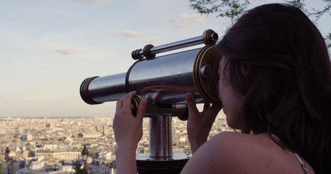 Tourist Girl looking through Binoculars at Paris cityscape view at sunset from Sacre Coeur viewpoint enjoying European summer holiday travel vacation adventure
