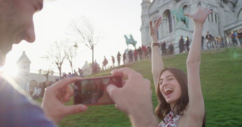 Tourist man taking photograph of girlfriend at Sacre Coeur Paris girl lifts arms up in excitement Man using smartphone camera in city enjoying summer holiday European vacation travel adventure