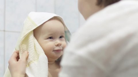 Caring mother wipes her child with a towel after washing, a cute baby holds a toy in his hand, close-up