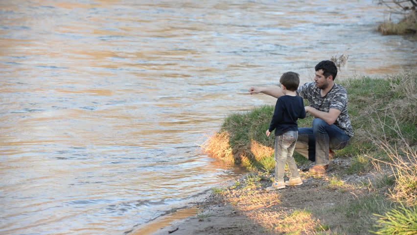 Father and son throwing rocks into the river. Dad and son playing by the river
