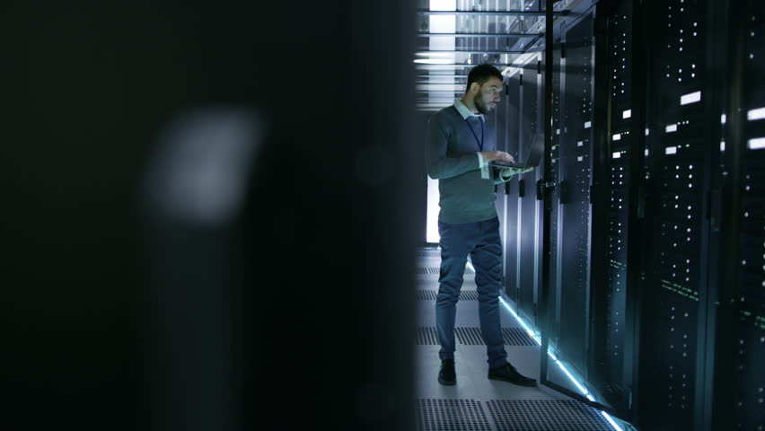 IT Technician Works on Laptop in Big Data Center full of Rack Servers. He Runs Diagnostics and Maintenance, Sets System Up. Shot on RED EPIC-W 8K Helium Cinema Camera. Royalty-Free Stock Footage #25116920