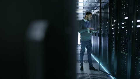IT Technician Works on Laptop in Big Data Center full of Rack Servers. He Runs Diagnostics and Maintenance, Sets System Up. Shot on RED EPIC-W 8K Helium Cinema Camera.
