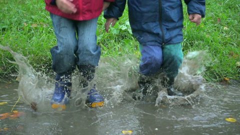 Two boys jumping in autumn muddy puddle together, slow motion 250 fps