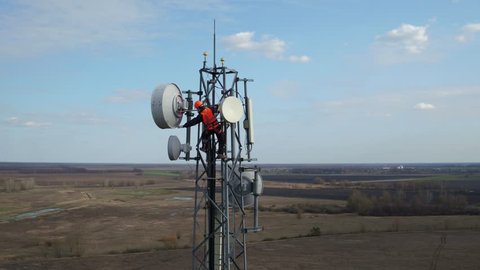 man working on radio telecommunication tower, radio master works at great heights of tv tower, industry of telecommunication engineering, drone flying around outdoor repeater base station tower