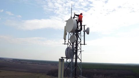 worker servicing cellular antenna in front of sunlight, drone view of telecommunication antenna system, technician working on top of cellular antenna