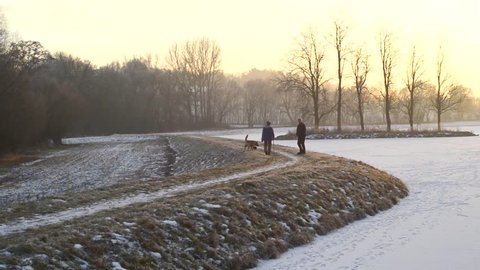 Seniors walking away with a dog, sunset winter snow landscape lake