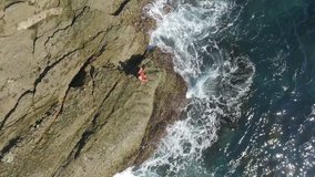 Yoga teacher doing yoga on the rock in the sea. Beautiful waves splashing on the cliffs in Laguna Beach California . Aerial view from the drone. 