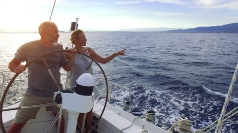 Mature adult couple having good time sailing on a sailboat in the blue ocean on a sunny day on their circumnavigation