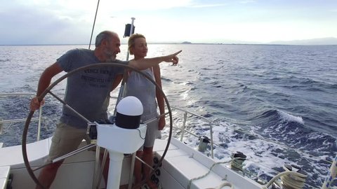 Mature adult couple having good time sailing on a sailboat in the blue ocean on a sunny day on their circumnavigation