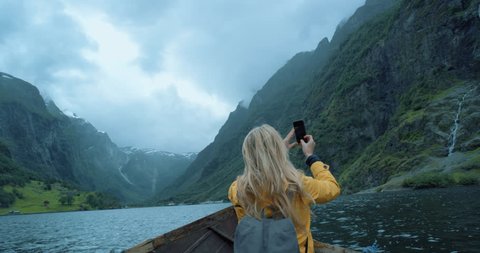 Brave Woman taking photograph in stormy weather on Fjord Norway with smartphone photographing scenic landscape nature background view enjoying vacation travel adventure
