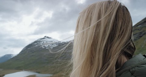 Close up portrait of beautiful young woman in nature with blonde hair blowing in wind looking at mountain view Hiker Girl in Norway Slow Motion