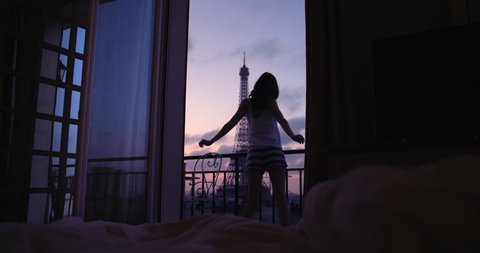 Young tourist woman stretching at sunrise on hotel terrace with view of Eiffel Tower Paris arms raised enjoying european travel adventure celebrating beautiful city