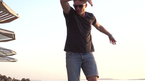 High Angle of Young Caucasian Man Dancing Happily on the Beach Near the Sunshade. Man Performing a Victory Dance on the Sunset. Elated Male on a Resort