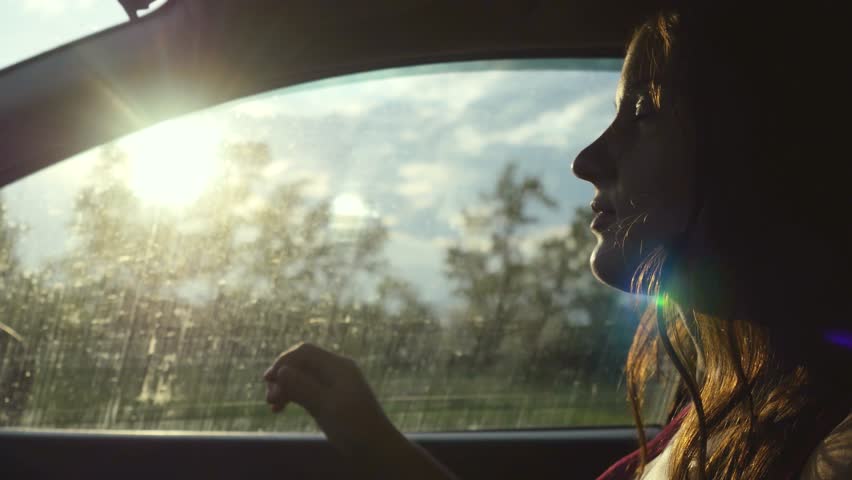 Happy young woman sitting in car passenger looking out window on sunny day enjoying rural car ride and singing song. Trip. Vacation. 3840x2160