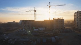 Construction site with a bird's eye on the Sunset. Video shooting with drone. Tower crane, excavator and sand. Flying over the construction site. The construction of the plant in the city.