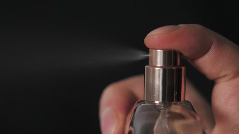 close up of handsome young business man using perfume or deodorant on black background macro