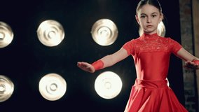 The young girl in red dress dancing cha-cha-cha on stage in bright light