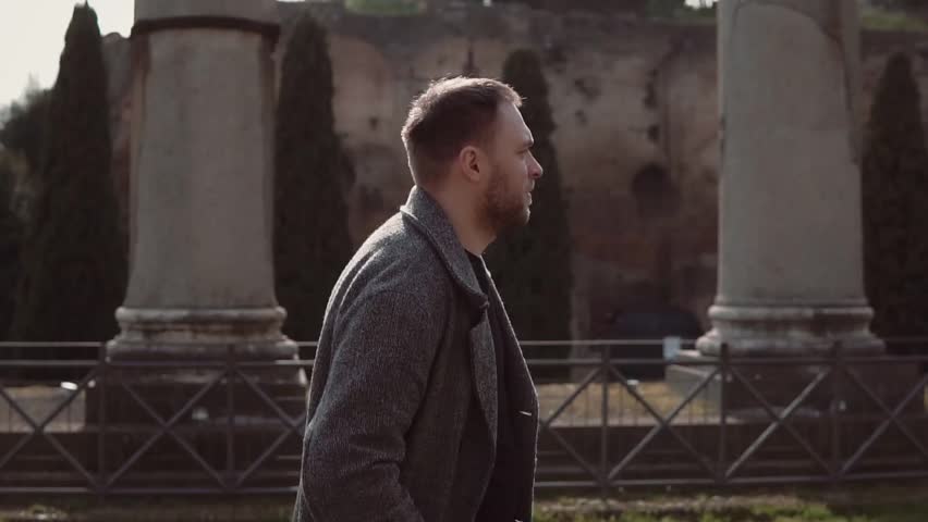 Handsome man walks on ruins of Rome, Italy. Guy does up hair, explores the architecture of Roman forum. Slow motion.