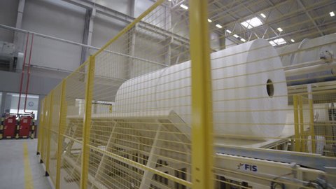 KAZAN, TATARSTAN/RUSSIA - JUNE 08 2015: Motion along big white paper rolls on machine behind yellow grid in toilet paper production workshop on June 08 in Kazan
