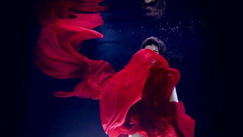 Beautiful young girl dancing underwater in a red dress. Slow motion. Flying in the water column.