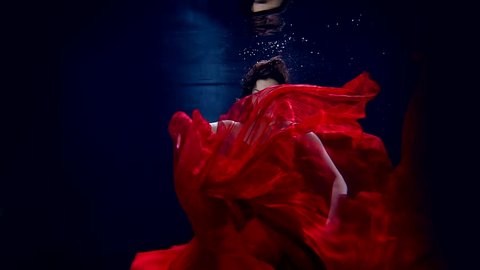 Flight in weightlessness of the underwater world of the young beautiful girl in elegant red dress.
