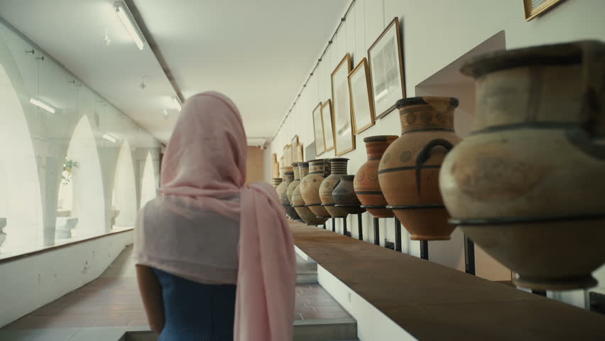 Woman in long dress walking in museum with clay pots