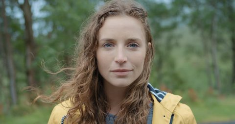 Close up portrait of Young Woman Smiling in nature with wet hair standing in rain Hiker Girl trekking cold stormy weather in Scotland Slow Motion