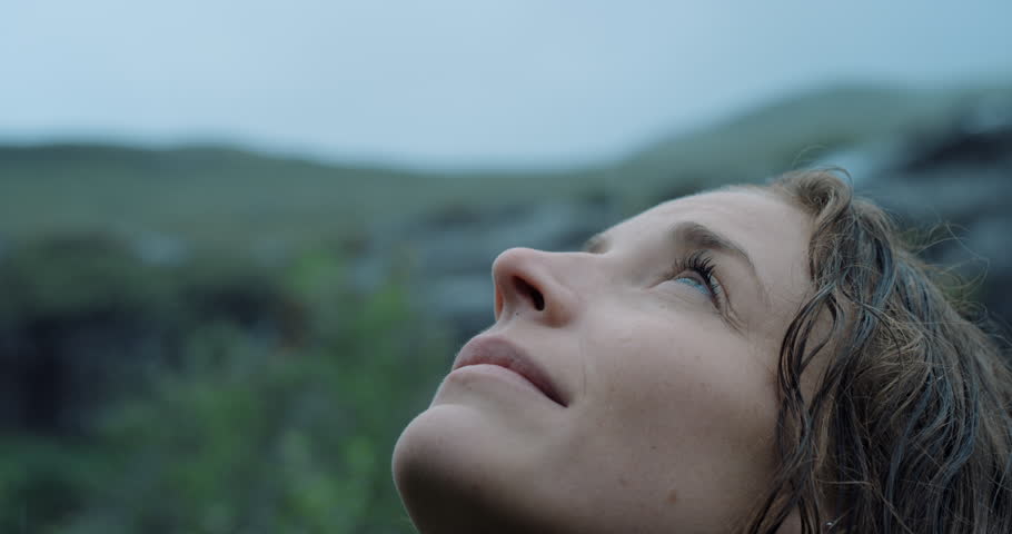 Close up portrait of Woman looking up at rain in nature with wet hair Hiker Girl trekking in Scotland Slow Motion