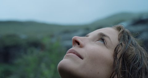 Close up portrait of Woman looking up at rain in nature with wet hair Hiker Girl trekking in Scotland Slow Motionの動画素材